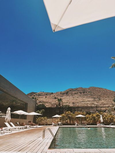 A resort pool lined with loungers and palms below a sunlit Tenerife hillside